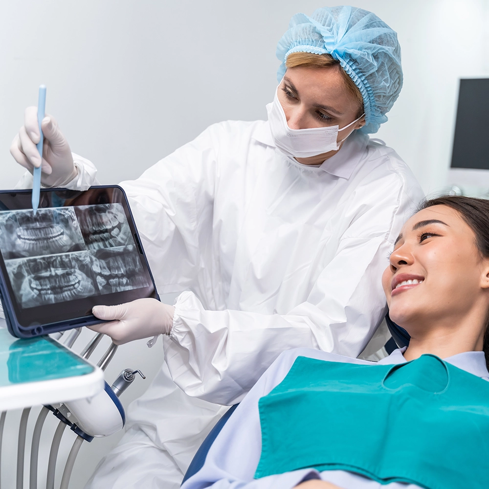 A patient lying in a dental chair while the dentist shows them dental X-rays.