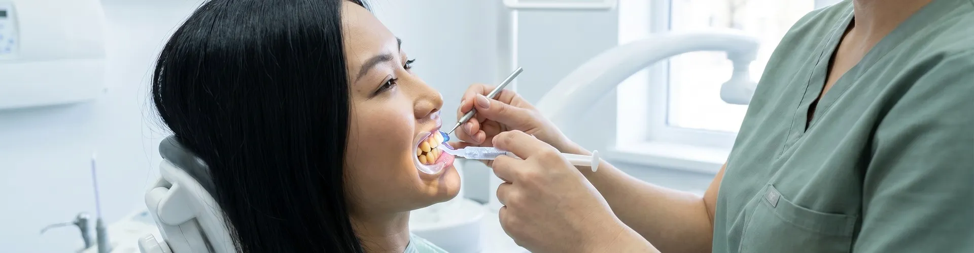 Dentist applying teeth whitening gel to a patient's teeth.
