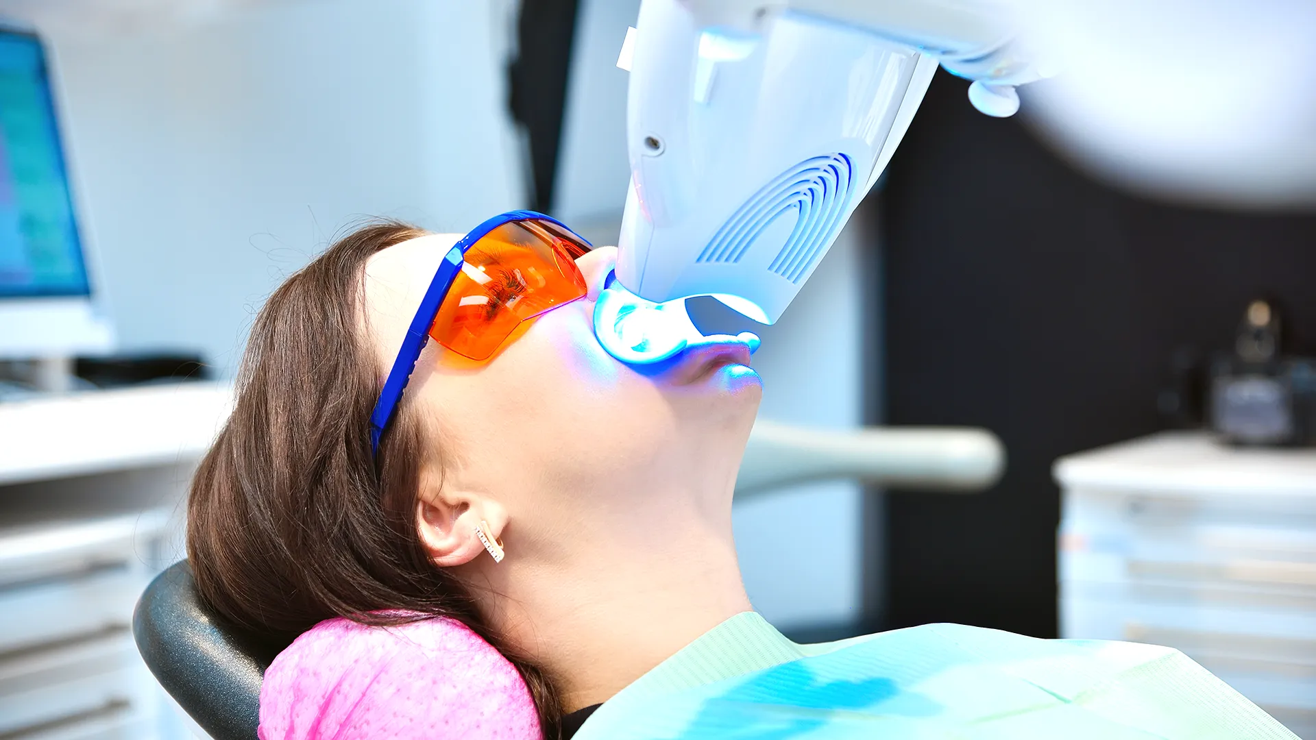 Woman receiving a teeth whitening treatment with ultraviolet light while wearing protective glasses.