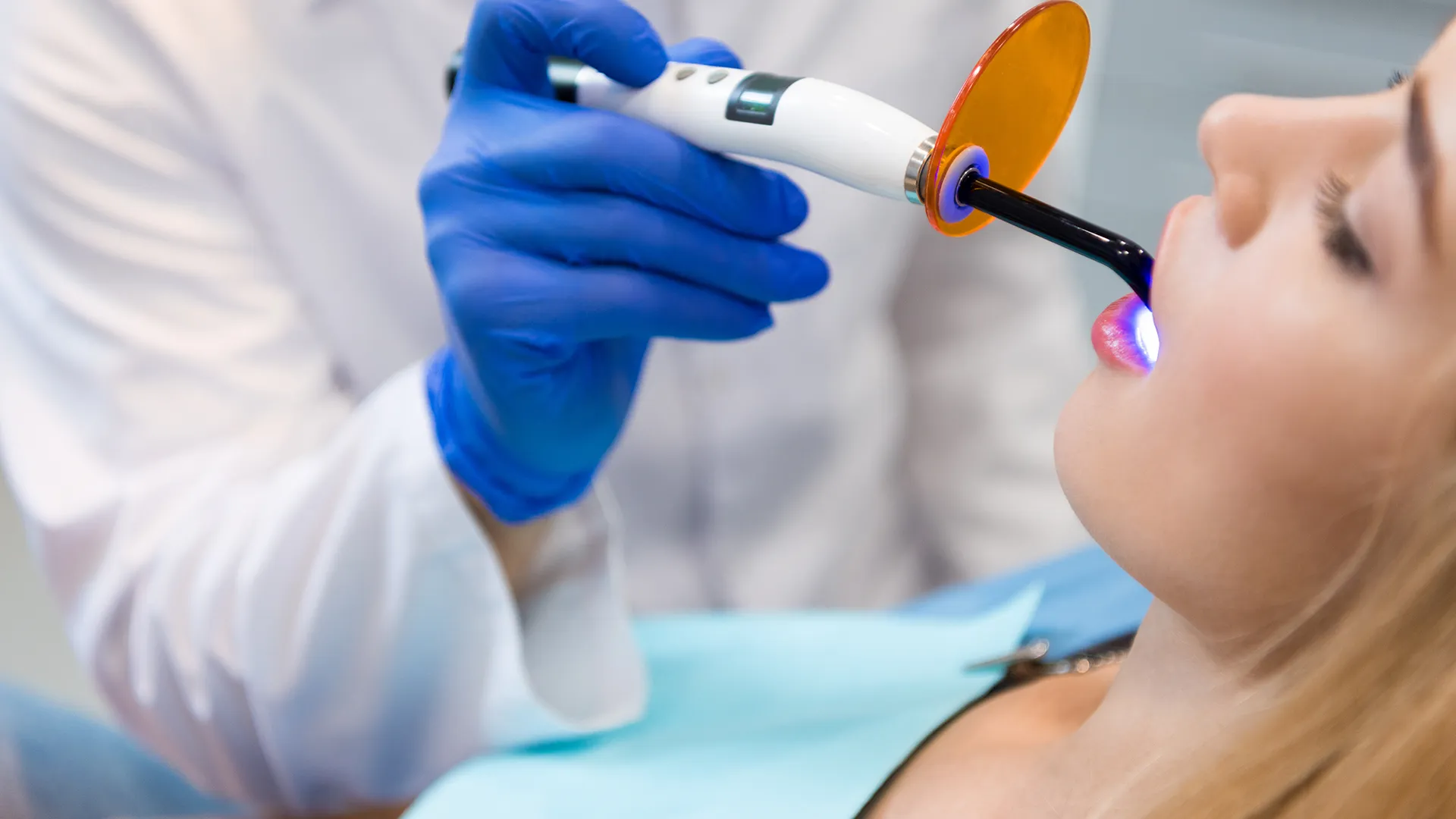 Dentist wearing blue gloves applying ultraviolet light to a patient's teeth.