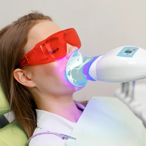 woman wearing orange glasses in dental chair with led light in her mouth