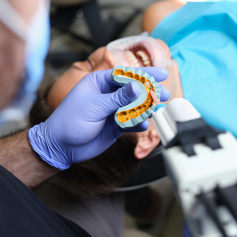Dentist wearing blue gloves working with a tooth mold.