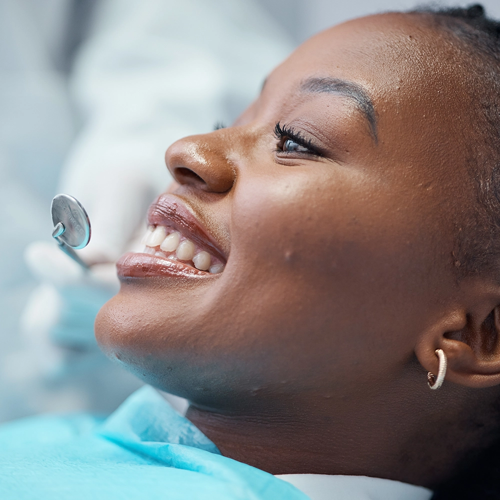 Woman smiling with a dental mirror held in front of her teeth.