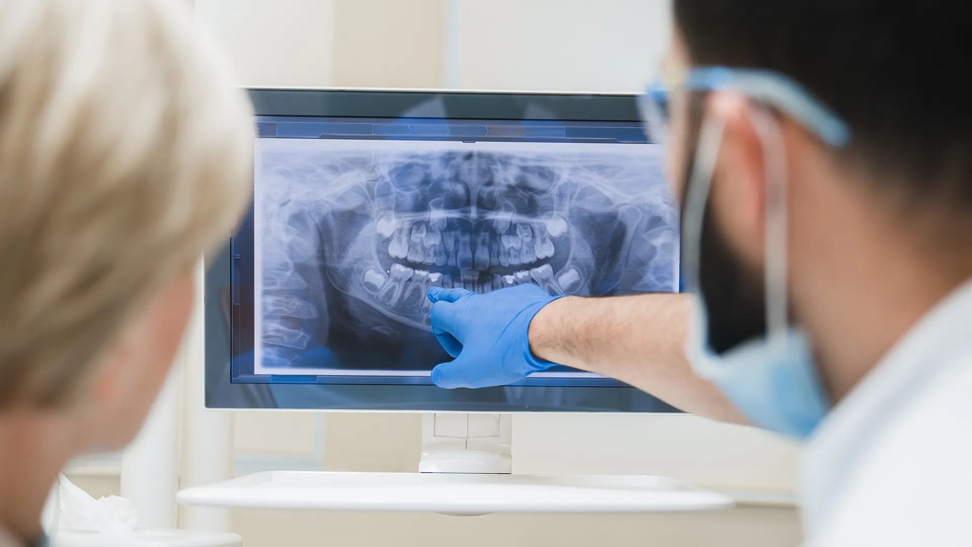 Dentist pointing to a screen displaying dental X-rays.