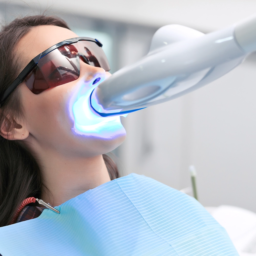 Woman receiving a teeth whitening treatment with ultraviolet light while wearing protective glasses.