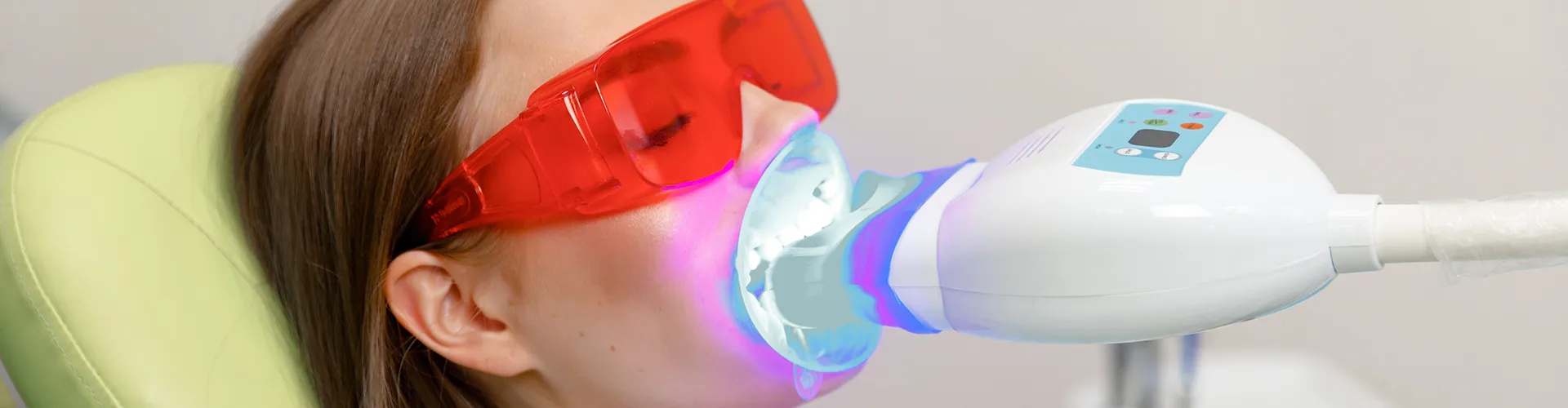 woman wearing orange glasses in dental chair with led light in her mouth