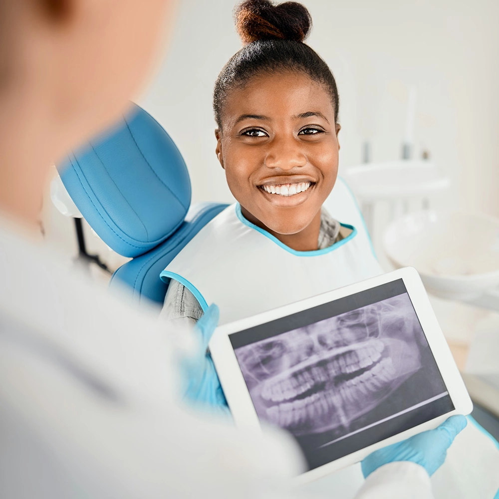 Woman seated in a dental chair smiling while the dentist holds dental X-rays.
