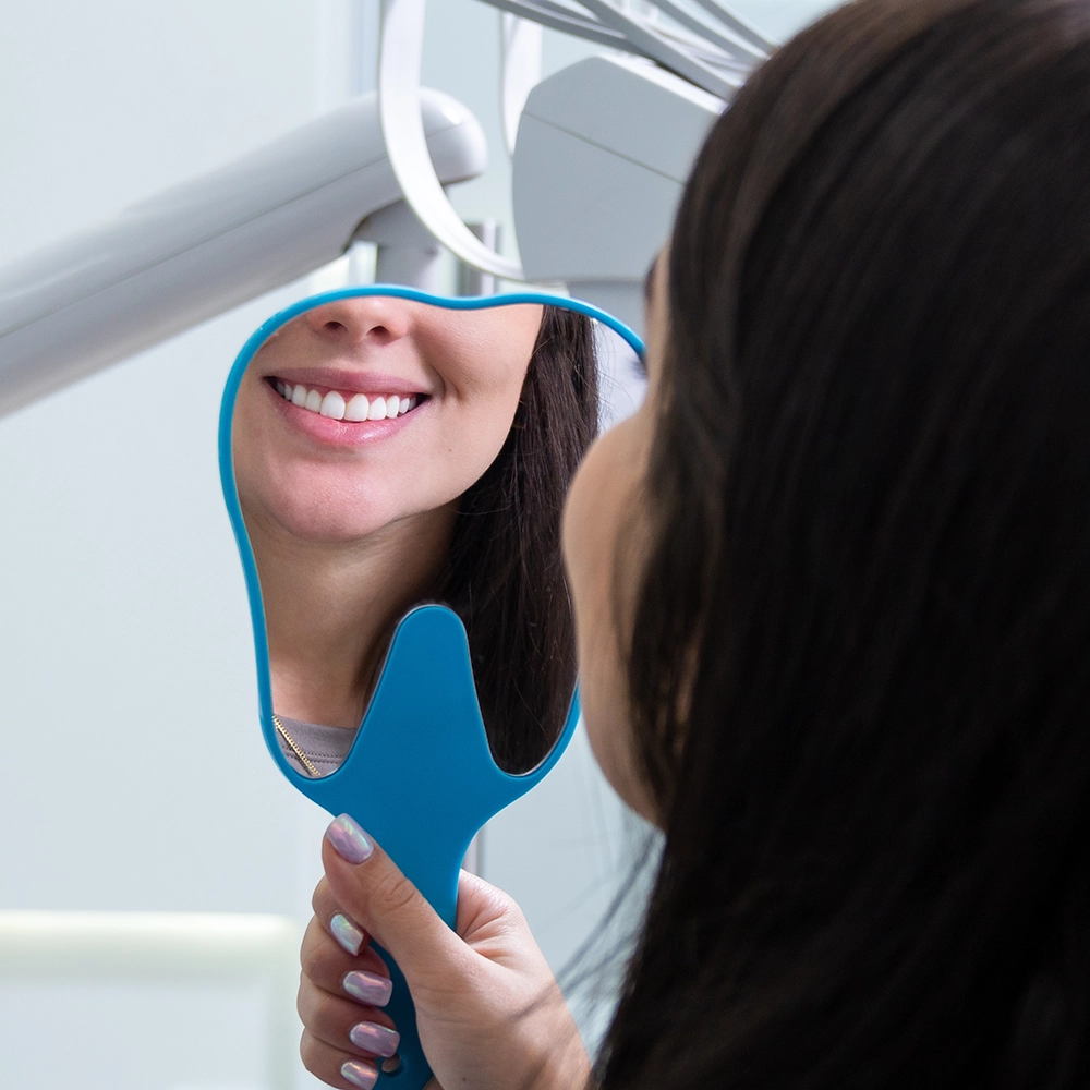 View from behind of a woman smiling, her smile reflected in the mirror she is holding.
