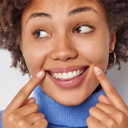 Smiling woman pointing to her teeth after a cosmetic smile makeover.