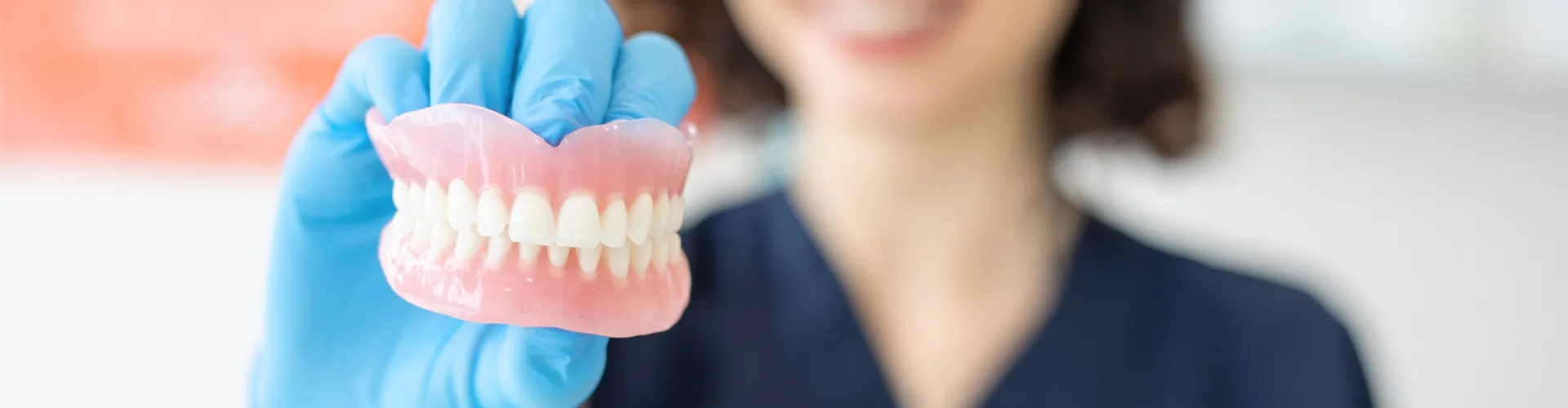 Gloved hand holding pair of dentures.