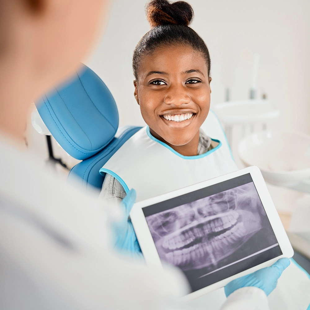 Woman seated in a dental chair smiling while the dentist holds dental X-rays.
