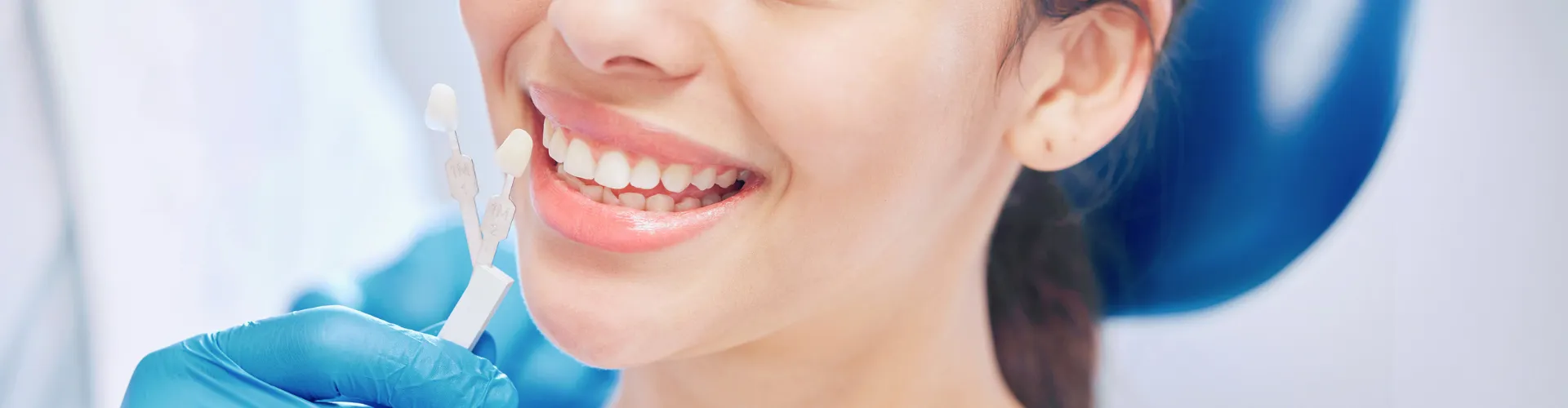 Gloved hand holding tooth shade-matching tool against woman's smile.