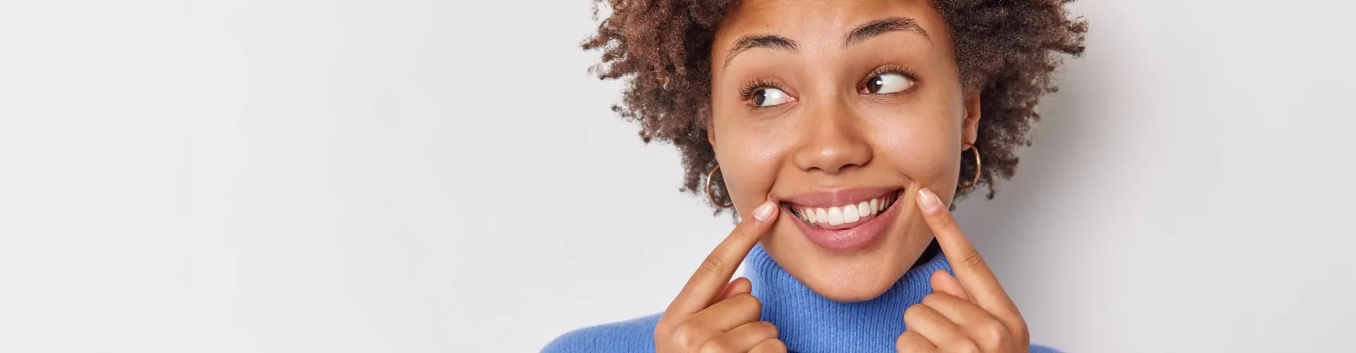 Smiling woman pointing to her teeth after a cosmetic smile makeover.