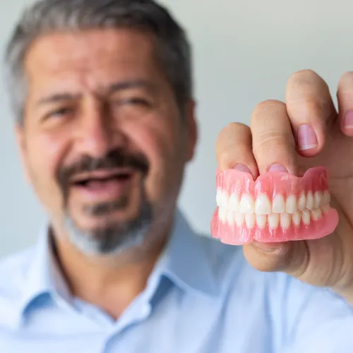 smiling man with no teeth holding upper and lower denture