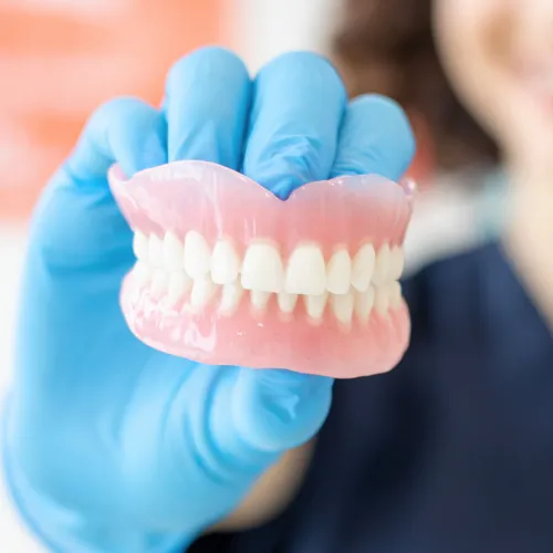 Gloved hand holding pair of dentures.