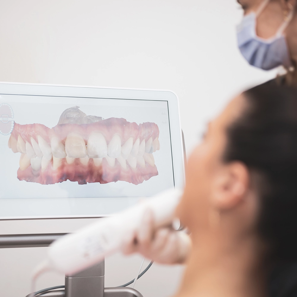 Woman seated in a dental chair looking at a 3D image of her teeth on a screen.