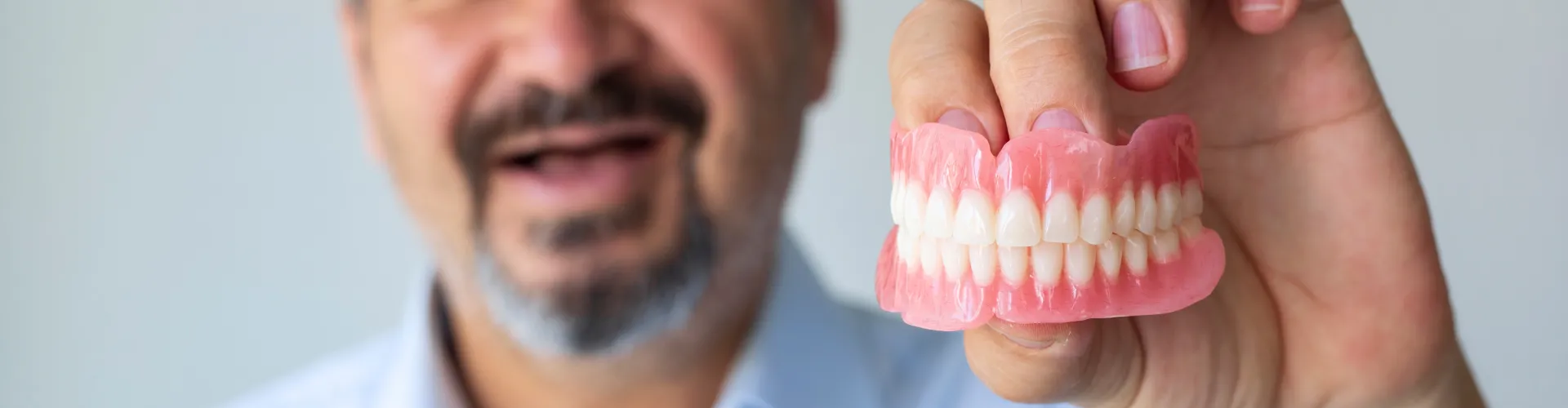 smiling man with no teeth holding upper and lower denture